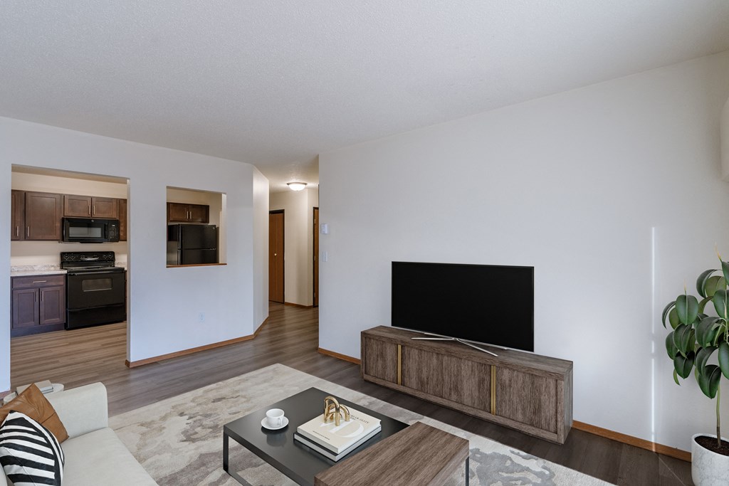 a living room with a couch and a tv and a kitchen. Fargo, ND Village West Apartments