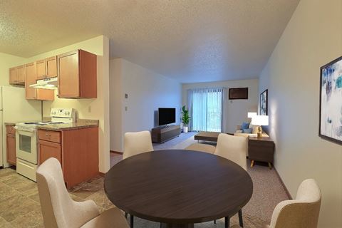 a dining area with a table and chairs and a kitchen in the background. Fargo, ND Village West Apartments