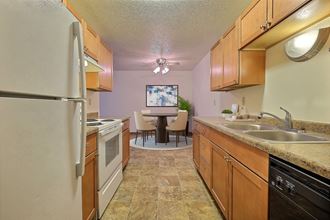 a kitchen with wooden cabinets and a dining room in the background. Fargo, ND Village West Apartments