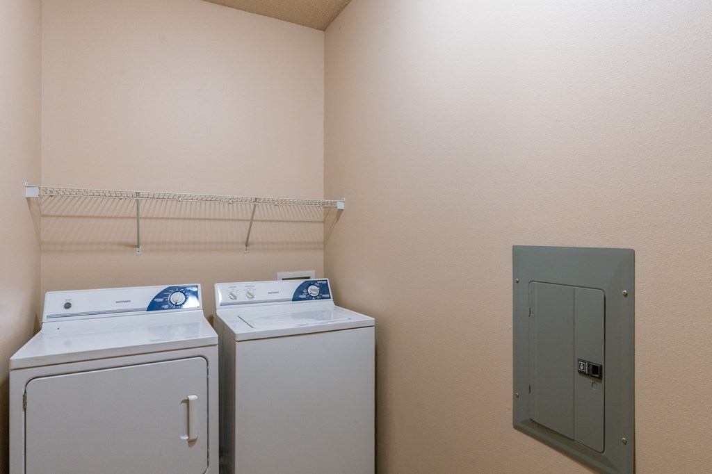 a laundry room with two washes and a dryer next to a green door. Fargo, ND West Lake Apartments