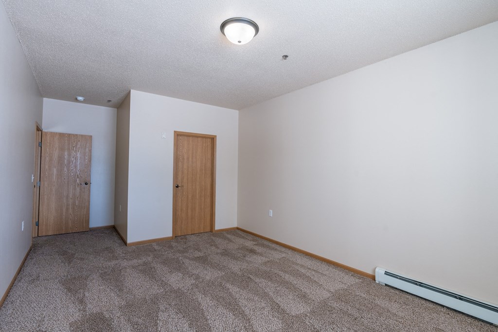 a bedroom with carpet and a door to a bedroom. Fargo, ND West Lake Apartments
