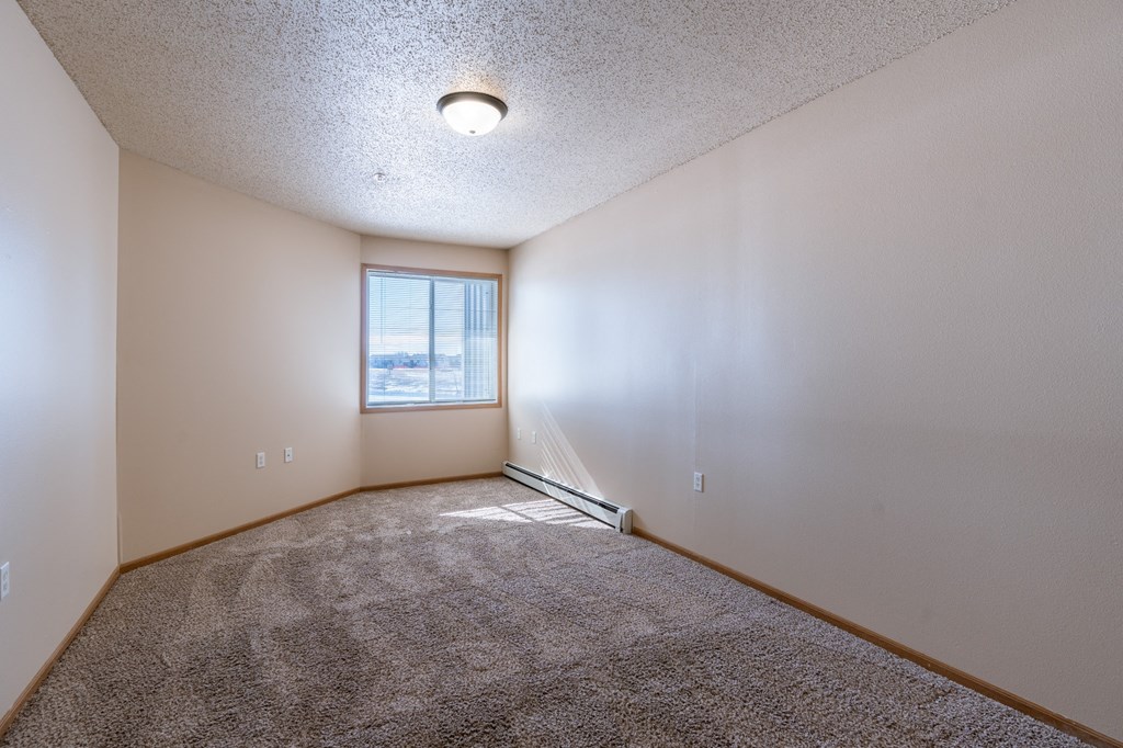 a bedroom with carpet and a window. Fargo, ND West Lake Apartments