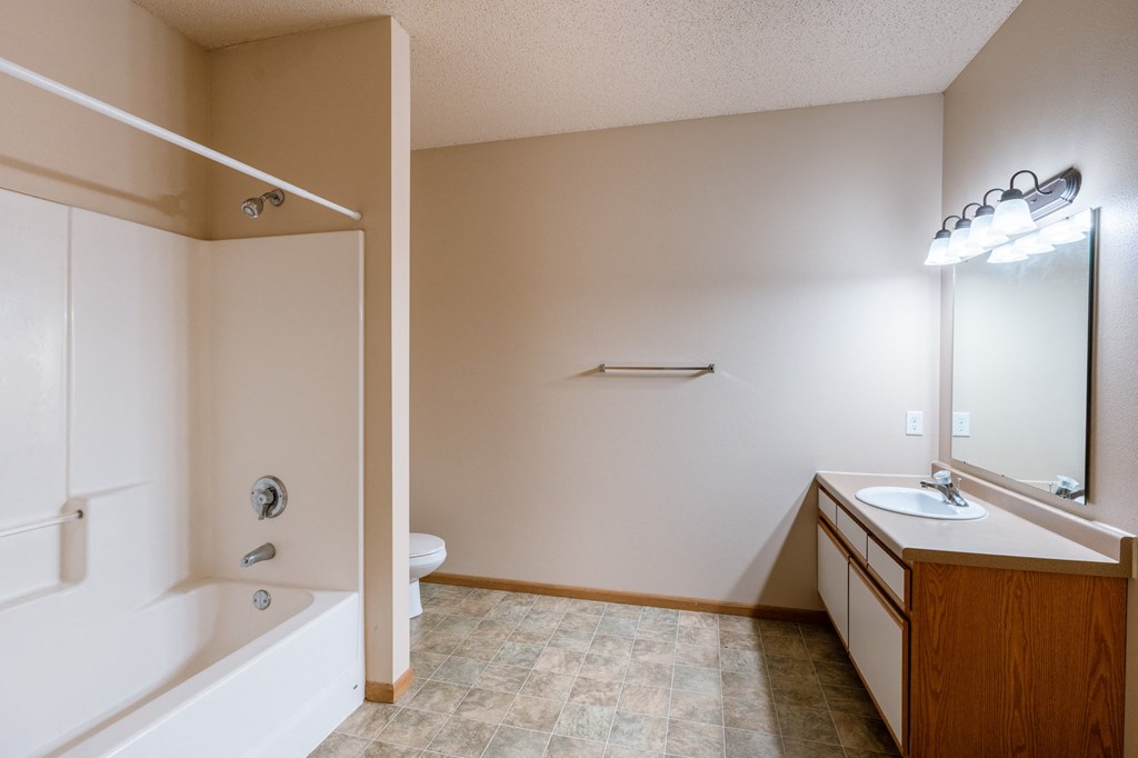 the view of a bathroom with a tub and a sink and a mirror. Fargo, ND West Lake Apartments