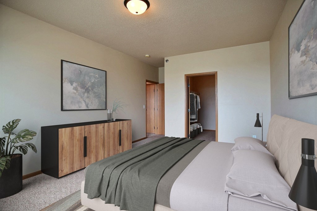 a bedroom with a bed and a dresser and a door to a bathroom. West Fargo, ND West Lake Apartments.