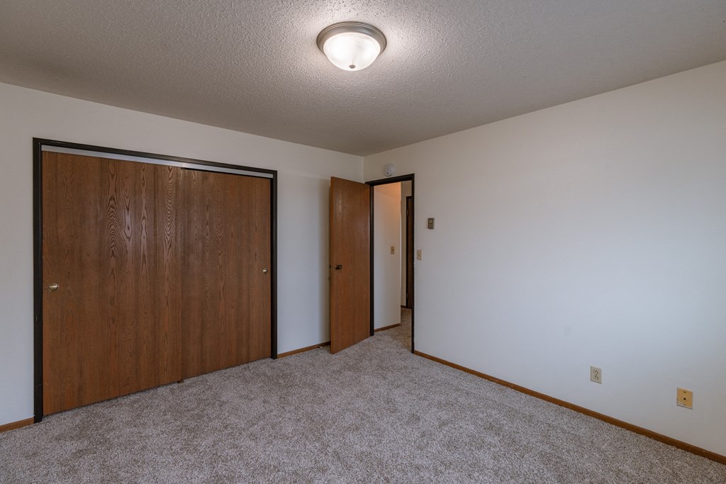 a room with a carpeted floor and a door to a closet. Fargo, ND West Oak Apartments.