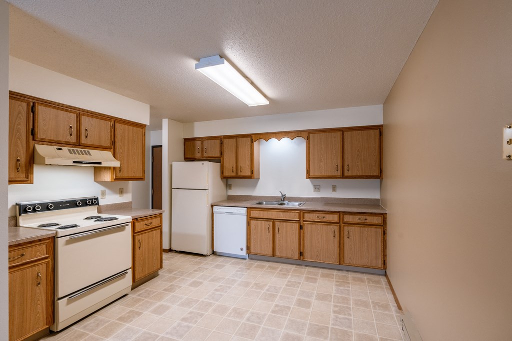 an empty kitchen with white appliances and wooden cabinets. Fargo, ND West Oak Apartments.