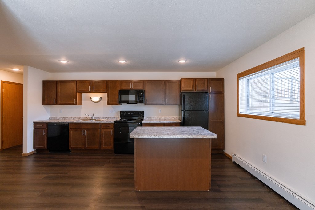 a kitchen with black appliances and an island with a window. Fargo, ND Westwood Apartments