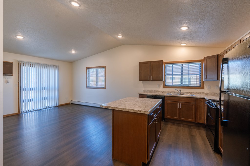 a kitchen with black appliances and a living room with two windows. Fargo, ND Westwood Apartments