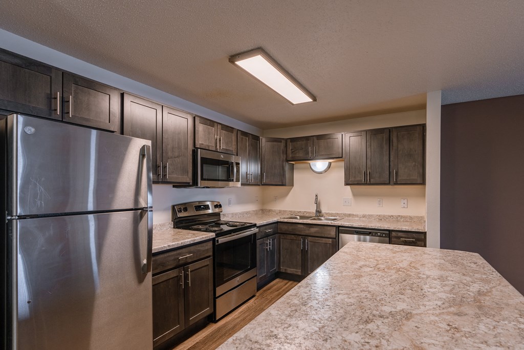 a kitchen with stainless steel appliances and dark wood cabinets. Fargo, ND Willow Park Apartments