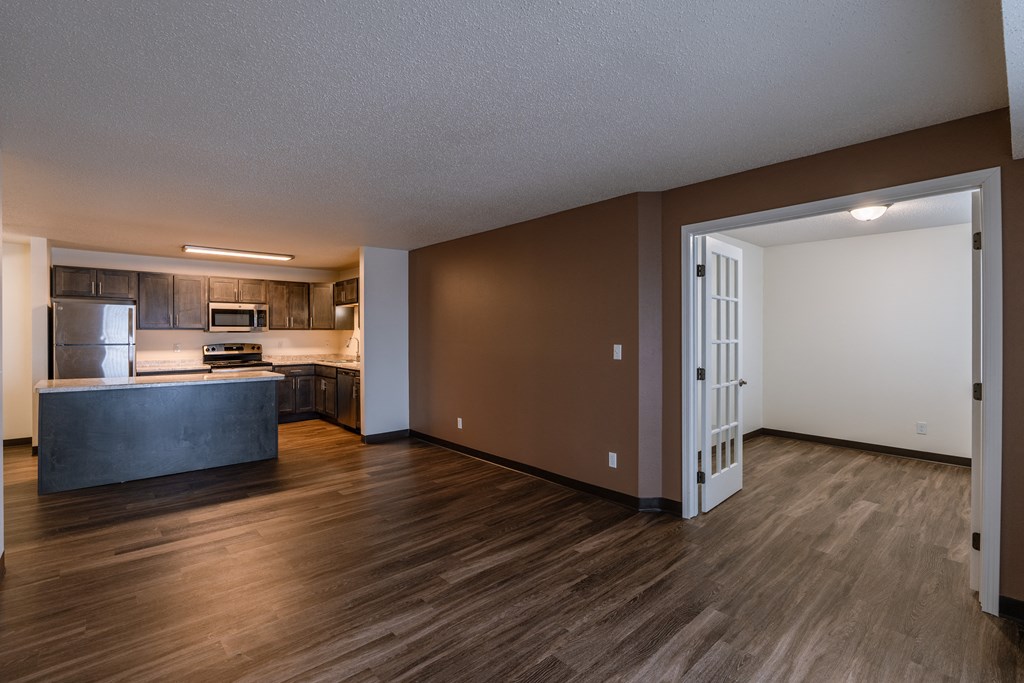 a living room with a brown wall and a kitchen in the background. Fargo, ND Willow Park Apartments