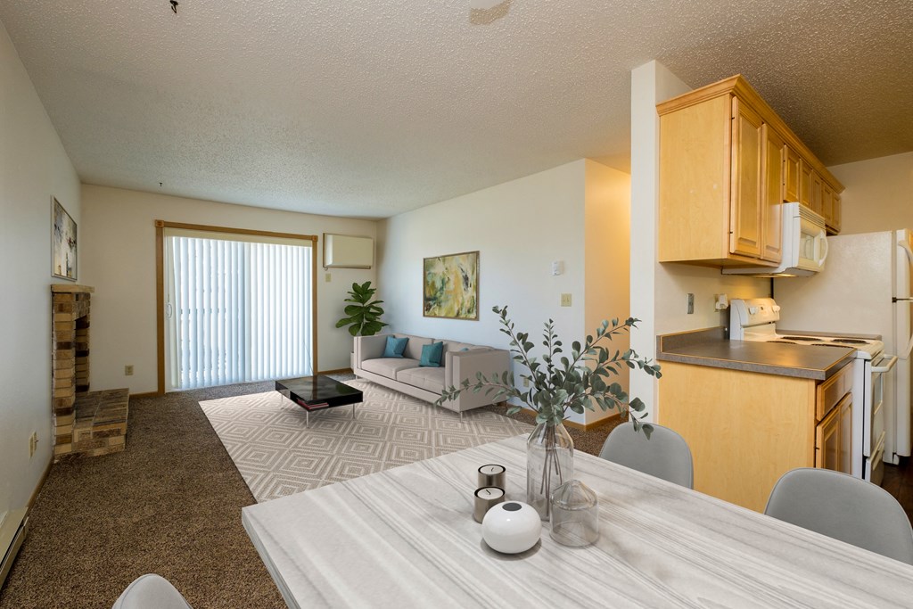 Fargo, ND Windgate Apartments. a dining room with a living room in the background. the dining room table has four chairs. the living room has a couch, coffee table, and a glass sliding door.