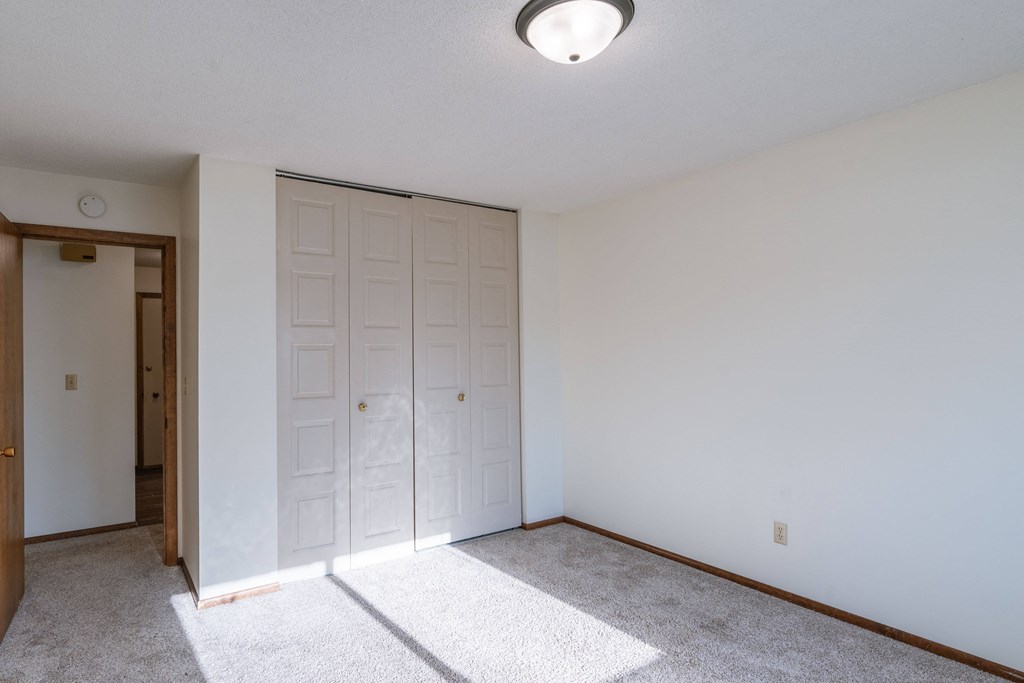 a bedroom with white walls and a door to a closet. Fargo, ND Windsor Apartments