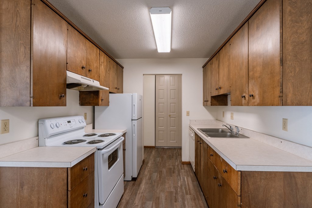 an empty kitchen with white appliances and wooden cabinets. Fargo, ND Windsor Apartments