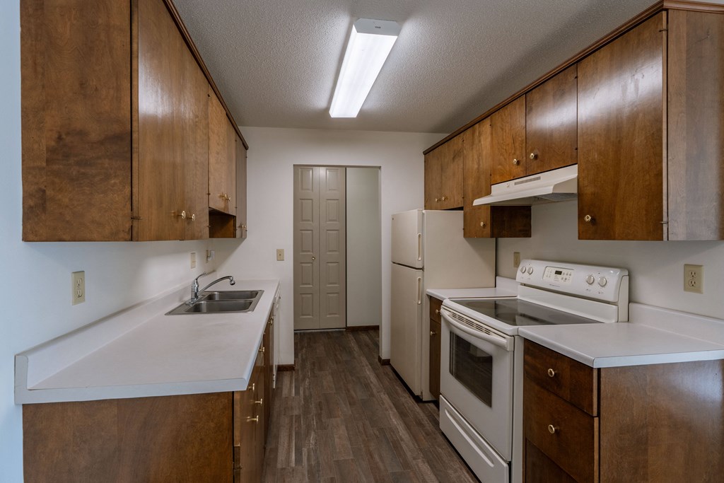an empty kitchen with white appliances and wooden cabinets. Fargo, ND Windsor Apartments