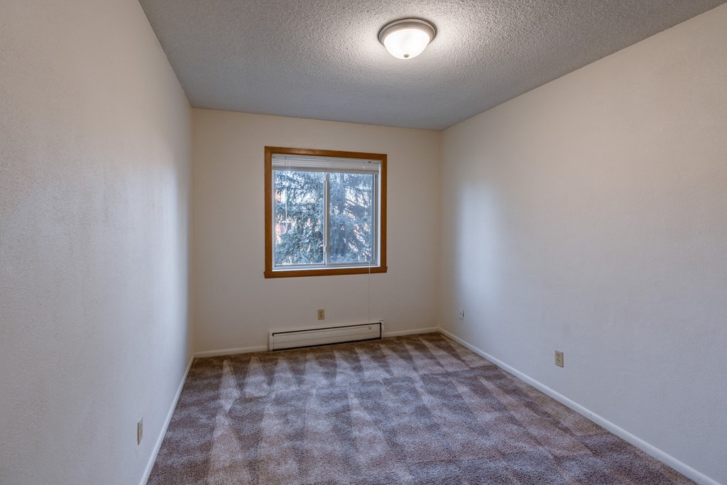 a bedroom with carpet and a window. Fargo, ND Woodland Apartments