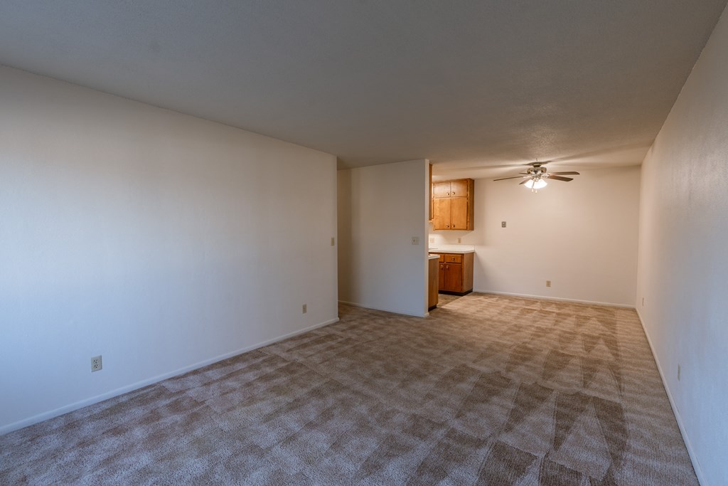 an empty living room with white walls and a ceiling fan. Fargo, ND Woodland Apartments