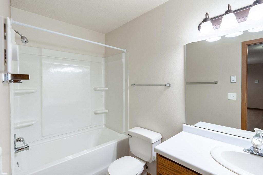 a bathroom with a shower toilet and sink and a mirror. Fargo, ND Briar Pointe Apartments