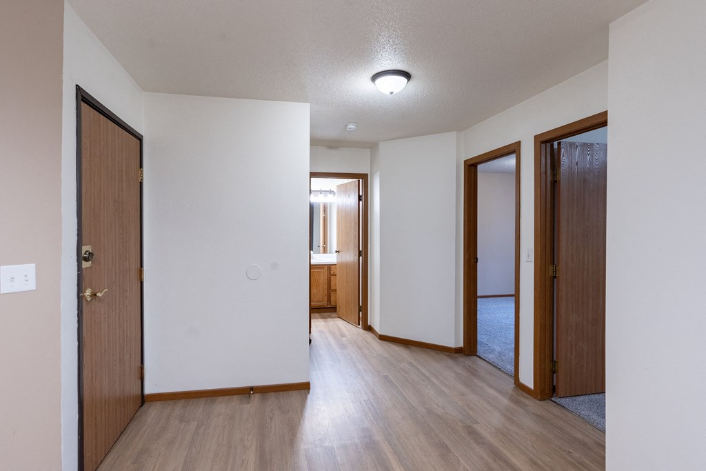 an empty living room and hallway with wood floors and white walls. Fargo, ND Briar Pointe Apartments