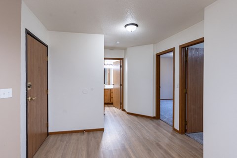 an empty living room and hallway with wood floors and white walls. Fargo, ND Briar Pointe Apartments