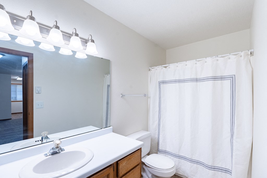 a bathroom with a large mirror and a sink and a toilet. Fargo, ND Brownstone Apartments