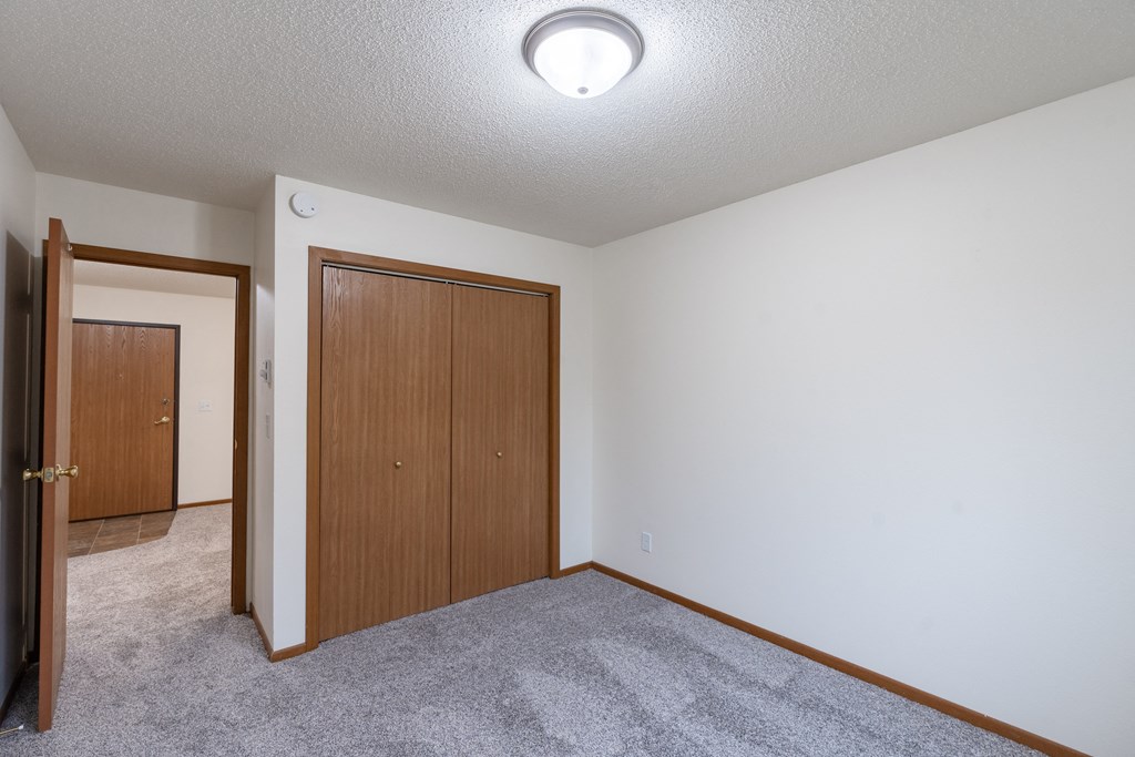 an empty living room with carpet and a door to a bedroom. Fargo, ND Brownstone Apartments