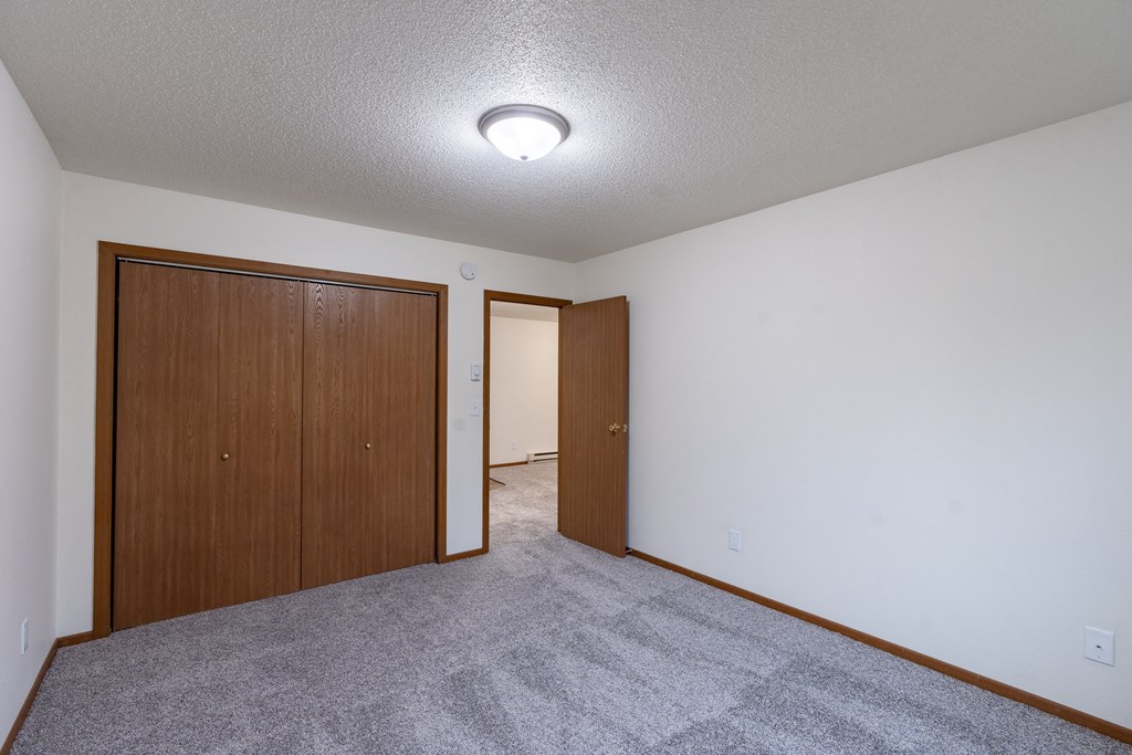 a living room with carpet and a door to a bedroom. Fargo, ND Brownstone Apartments