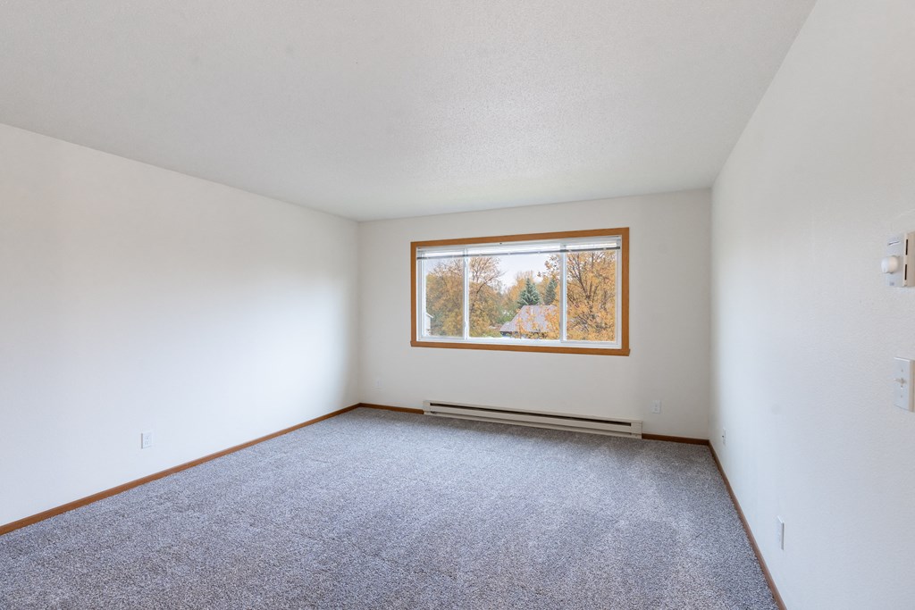 an empty living room with a window and carpet. Fargo, ND Brownstone Apartments