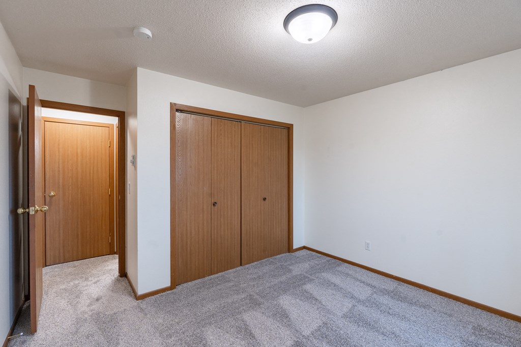 an empty living room with carpet and a door to a closet. Fargo, ND Brownstone Apartments