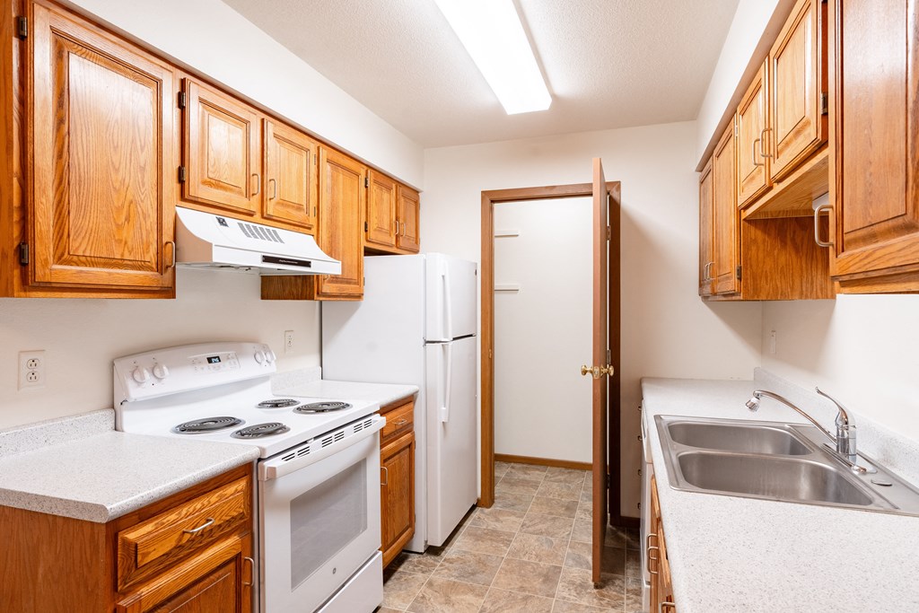 a kitchen with white appliances and wooden cabinets and a white refrigerator. Fargo, ND Brownstone Apartments
