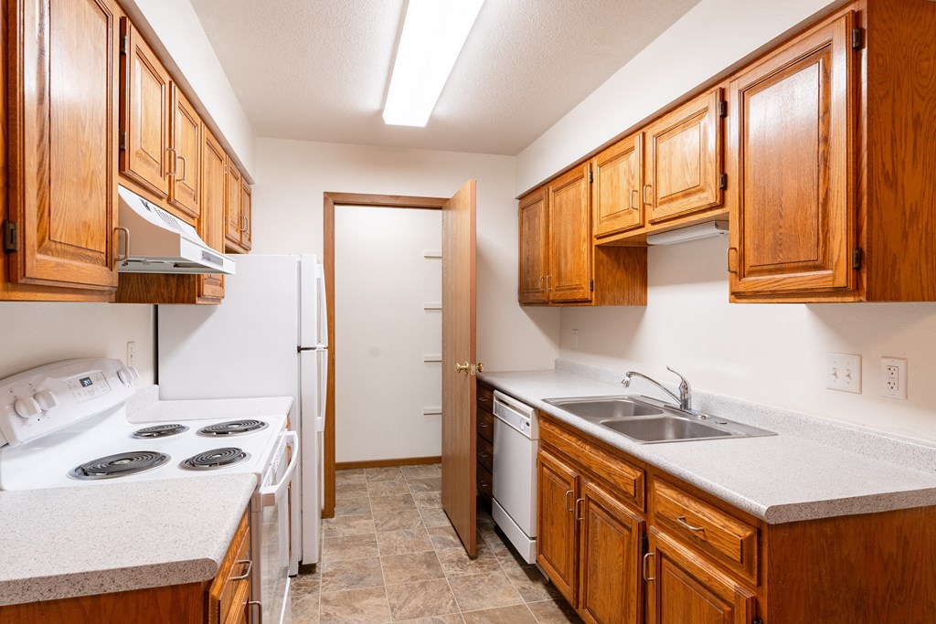 a kitchen with wood cabinets and white appliances and a sink. Fargo, ND Brownstone Apartments