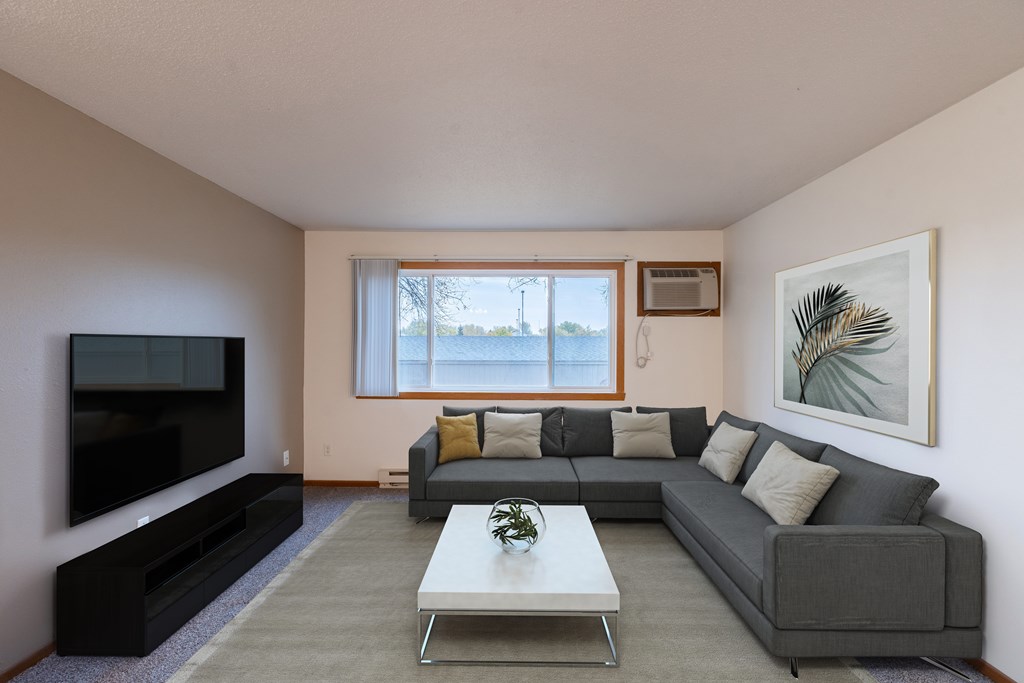 a living room with a gray couch and a coffee table and a television. Fargo, ND Brownstone Apartments
