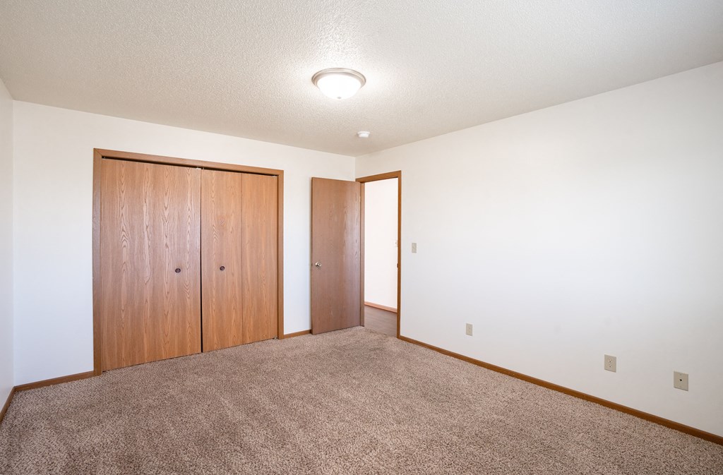 a bedroom  with a carpeted floor and a closet. Fargo, ND Carlton Place Apartments