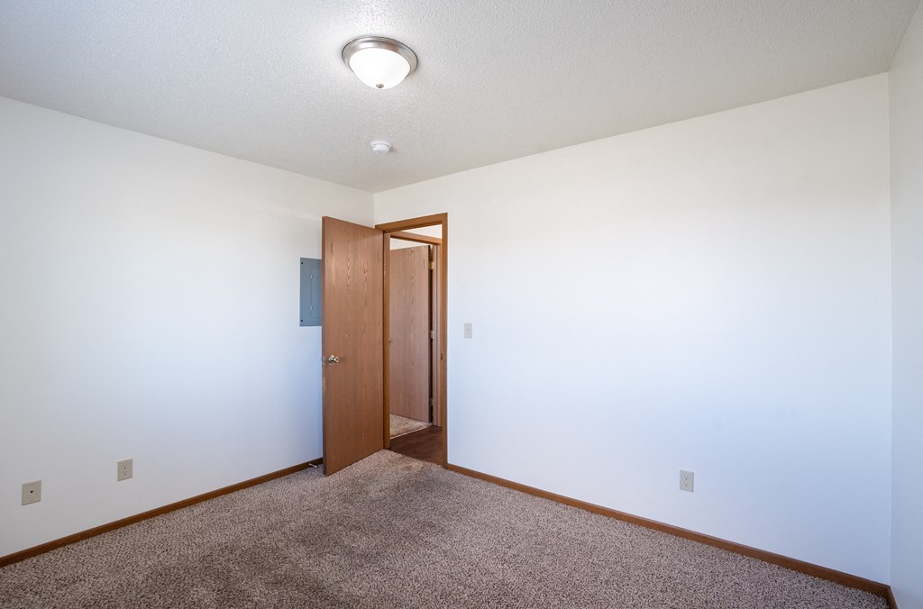 a bedroom with carpeted floor and a door to a hallway. Fargo, ND Carlton Place Apartments