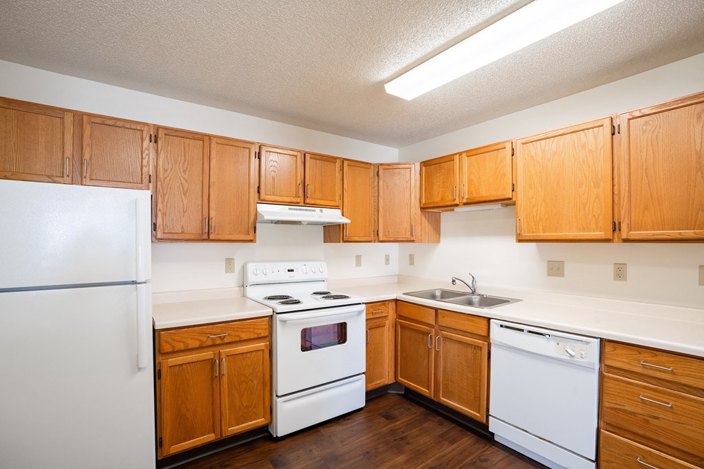 an empty kitchen with white appliances and wooden cabinets. Fargo, ND Carlton Place Apartments