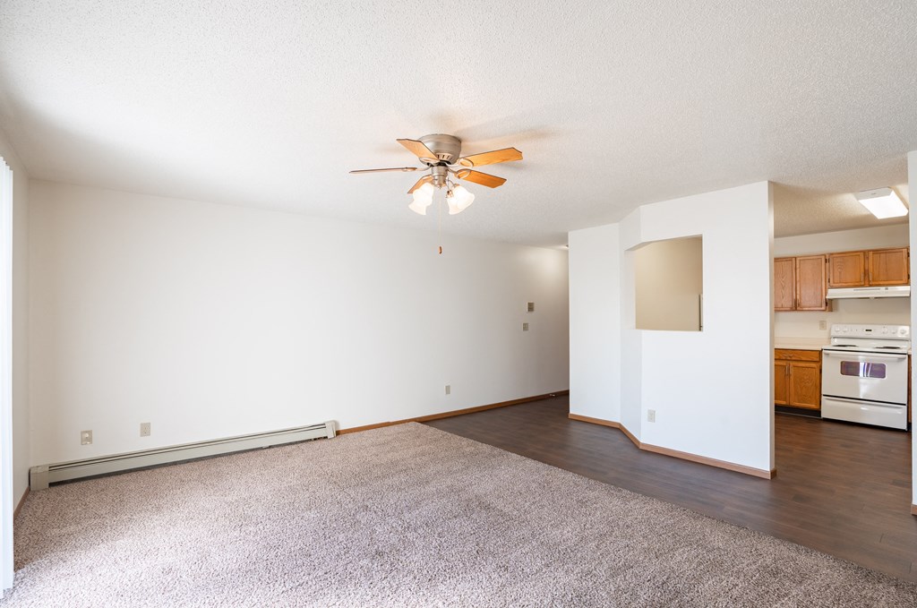 an empty living room with a ceiling fan and a kitchen. Fargo, ND Carlton Place Apartments