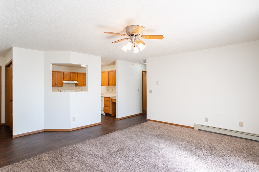 a living room with a ceiling fan and kitchen in the background. Fargo, ND Carlton Place Apartments