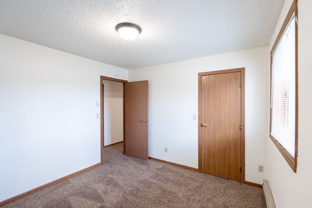 an empty living room with a door to a closet and a window. Fargo, ND Cedar Pointe Apartments
