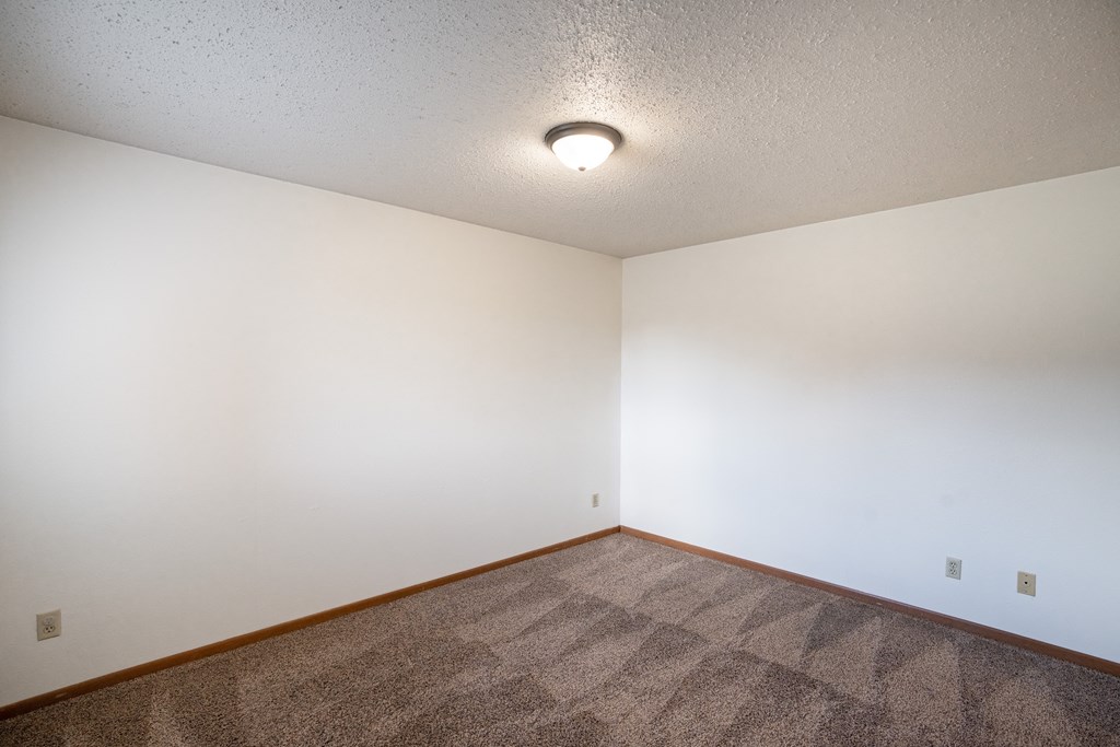 an empty living room with carpet and white walls. Fargo, ND Cedar Pointe Apartments