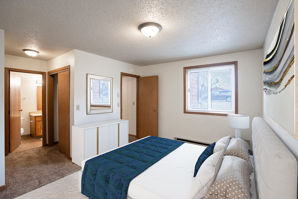 a bedroom with a white bed and a blue blanket. Fargo, ND Cedar Pointe Apartments