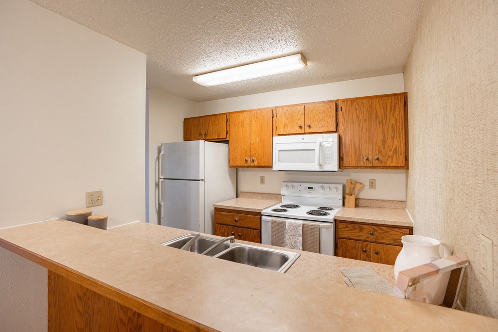 a kitchen with white appliances and wooden cabinets and a sink. Fargo, ND Cedar Pointe Apartments