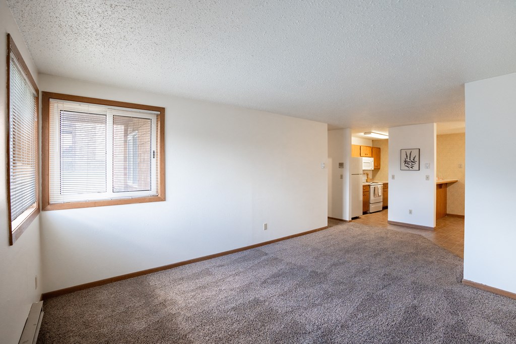 an empty living room with a large window and a carpeted floor. Fargo, ND Cedar Pointe Apartments