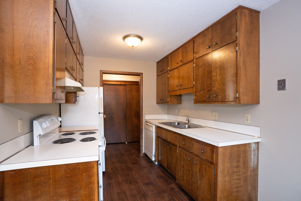 a kitchen with white counters and wooden cabinets and a stove and sink. Fargo, ND Country Club Apartments