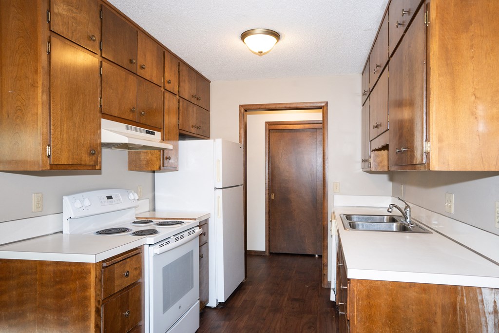 an empty kitchen with white appliances and wooden cabinets. Fargo, ND Country Club Apartments