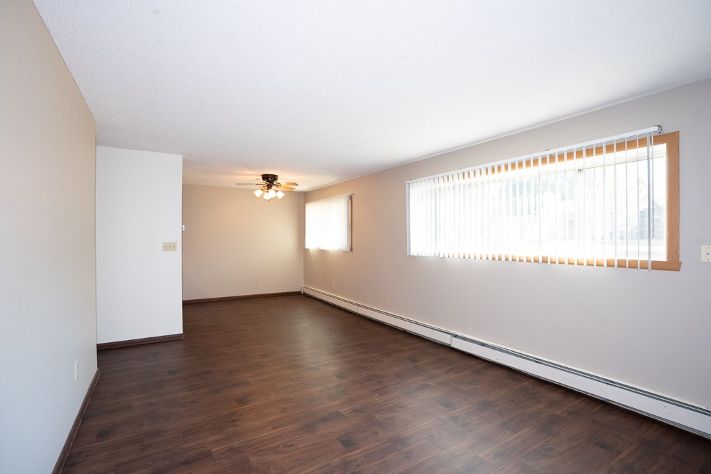 an empty living room with wood floors and a large window. Fargo, ND Country Club Apartments
