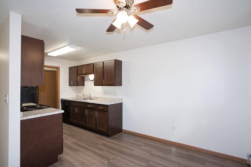 an empty kitchen with wooden cabinets and a ceiling fan. Fargo, ND Country Club Apartments