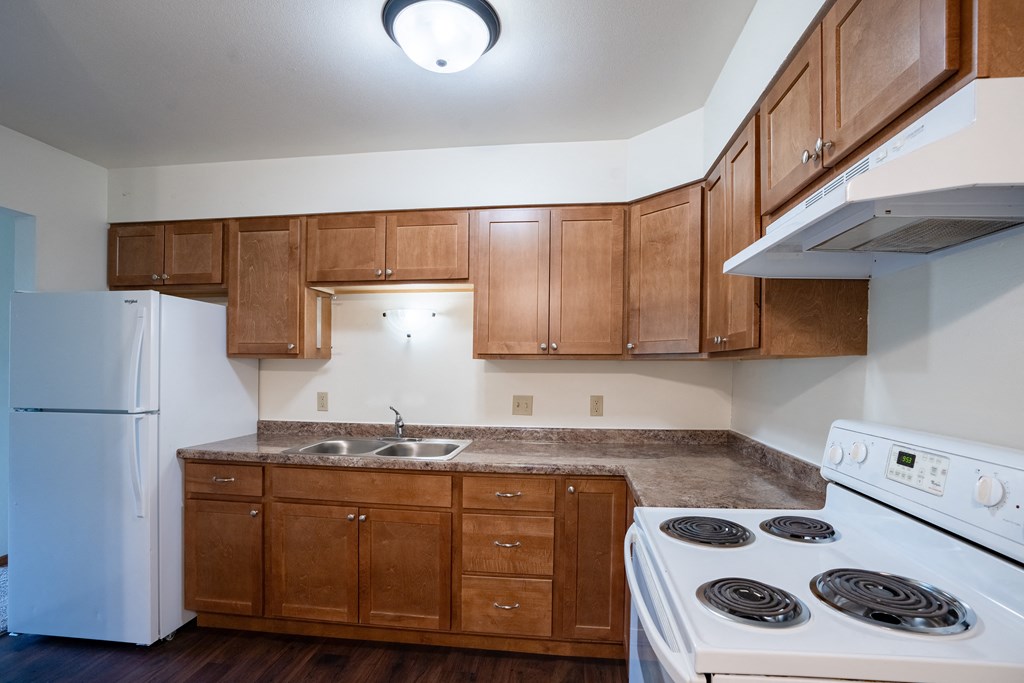 an empty kitchen with white appliances and wooden cabinets. Fargo, ND Crown Court 1 Apartments