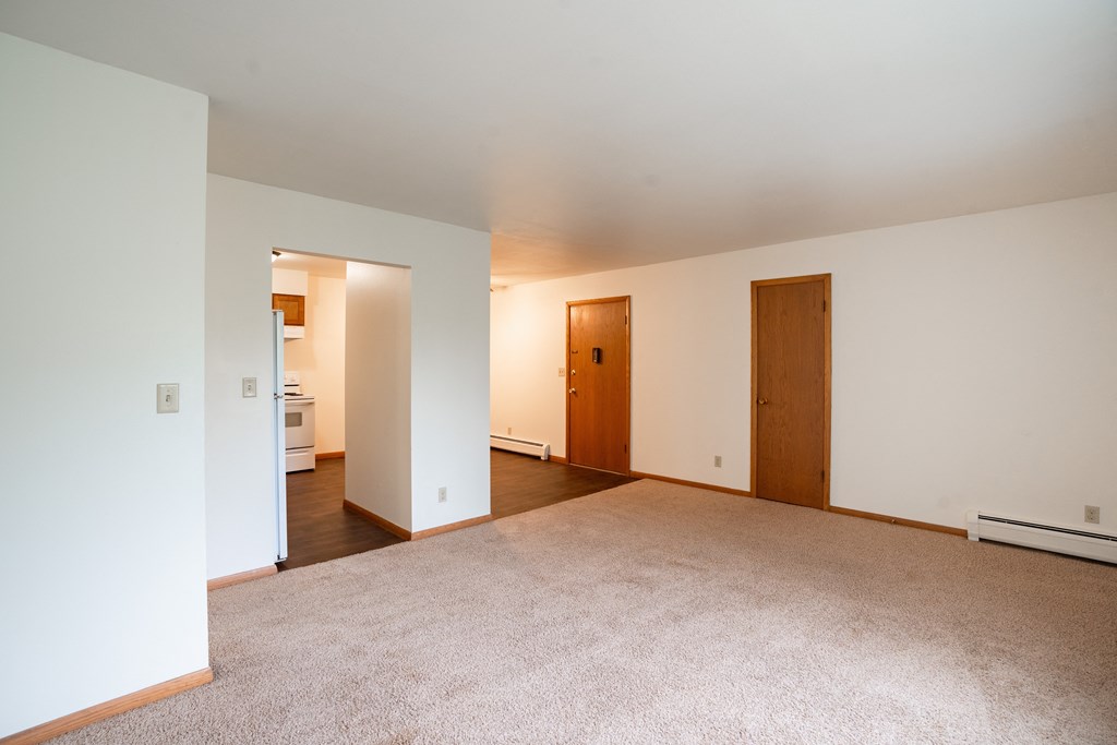 a living room with carpet and white walls and two doors. Fargo, ND Crown Court 1 Apartments