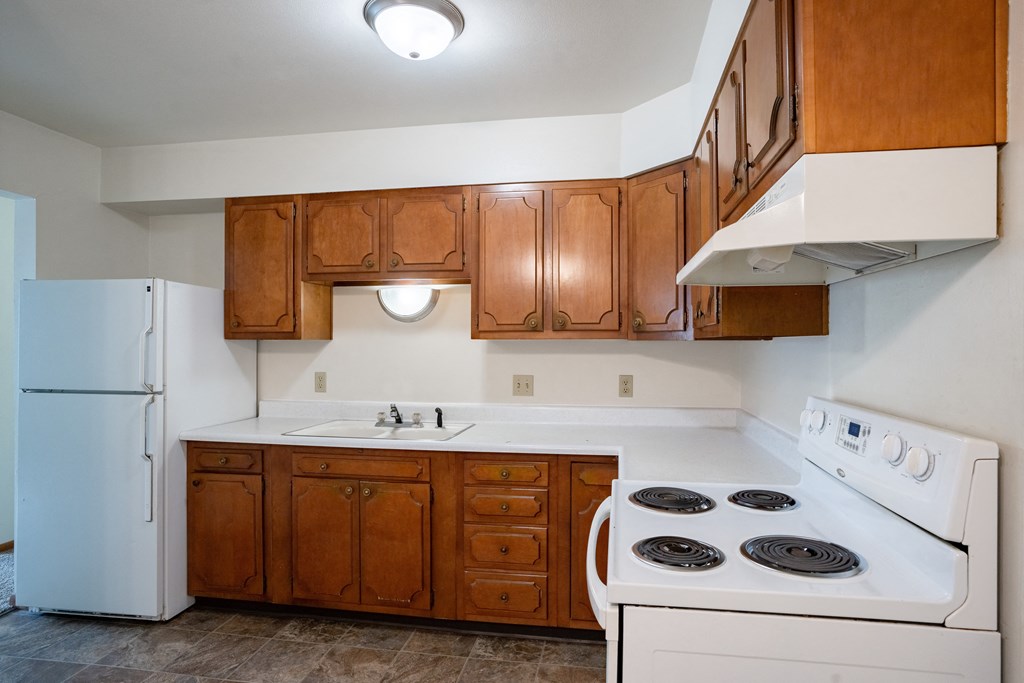 an empty kitchen with white appliances and wooden cabinets. Fargo, ND Crown Court 1 Apartments