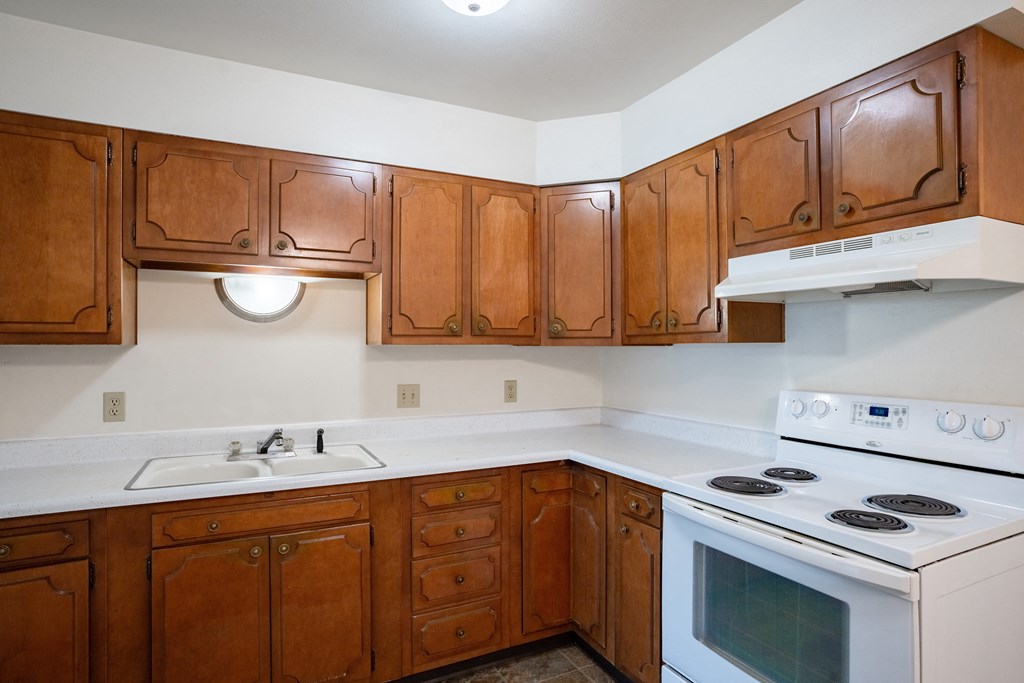 an empty kitchen with wooden cabinets and white appliances.  Fargo, ND Crown Court 1 Apartments