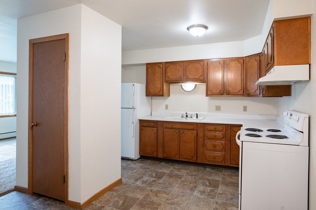an empty kitchen with white appliances and wooden cabinets